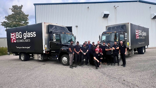 BG Glass Technologies team posing in front of two company delivery trucks outside the facility.